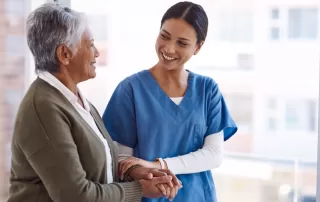 female caretaker in blue scrubs caring for and holding the hand of an elderly female patient