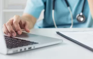 healthcare nurse working on a laptop with information on a clipboard