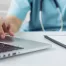 healthcare nurse working on a laptop with information on a clipboard