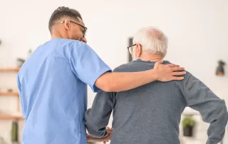male social worker assisting older man walk in his home