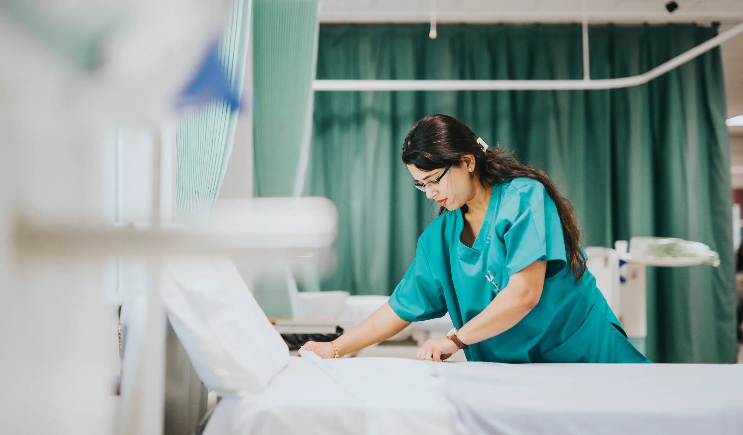 Nurse in teal scrubs preparing a hospital bed in a healthcare facility