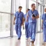 Four healthcare workers in scrubs walking in corridor.